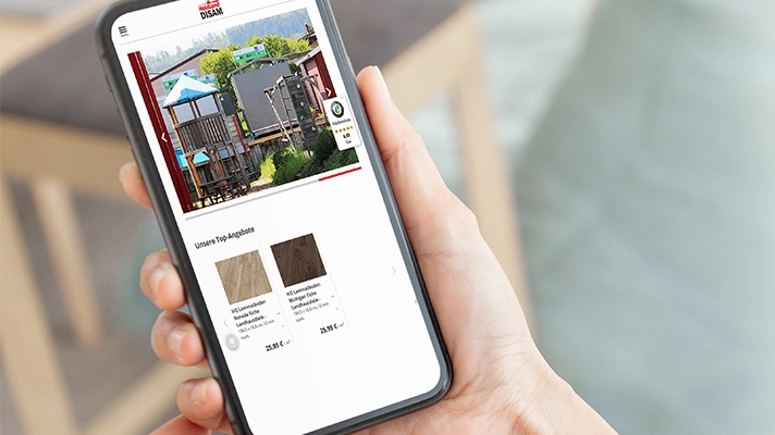 „Person hält Smartphone in der Hand und schaut auf die Website eines Holzfachhändlers mit Online-Shop.