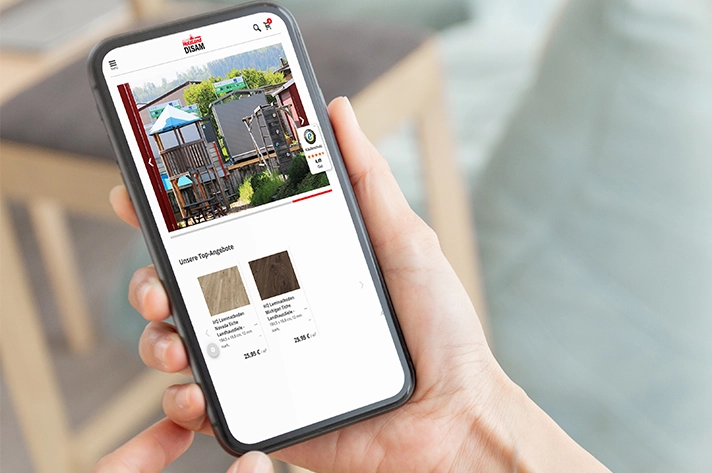 „Person hält Smartphone in der Hand und schaut auf die Website eines Holzfachhändlers mit Online-Shop.